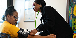 A faculty member takes the blood pressure of a female patient at the library