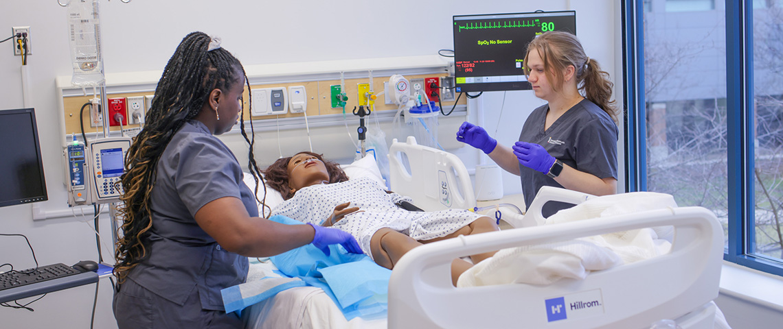 Two female students work together to care for a sim patient