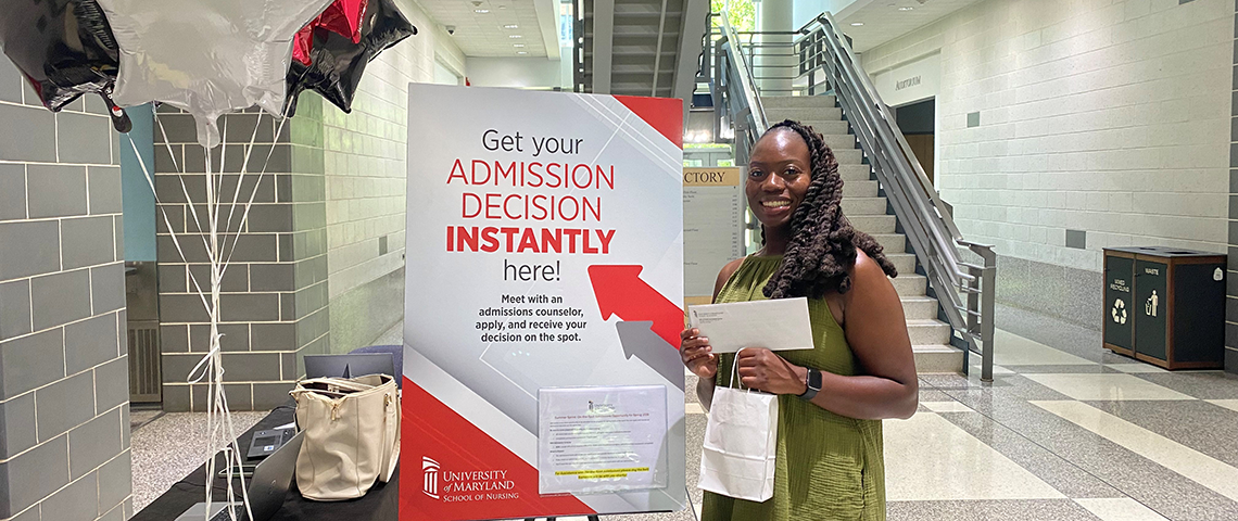 A smiling woman holds up a letter next to a sign that says 