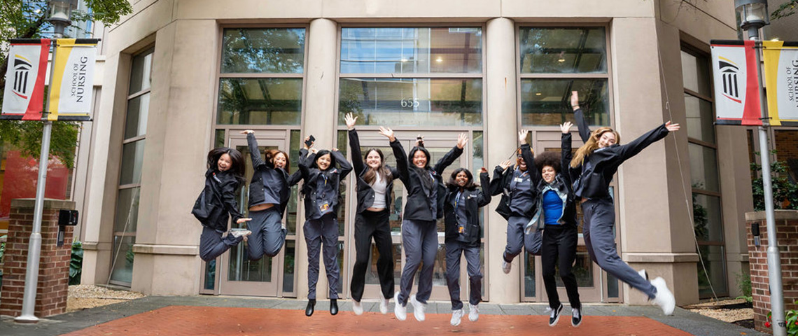 Students in scrubs jumping in front of the UMSON building