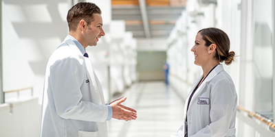 A man and woman in whitecoats are talking in a hospital hallway