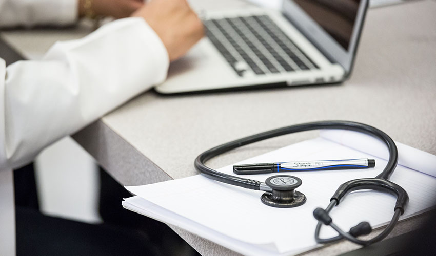 student typing on a laptop with a stethoscope and notebook next to them